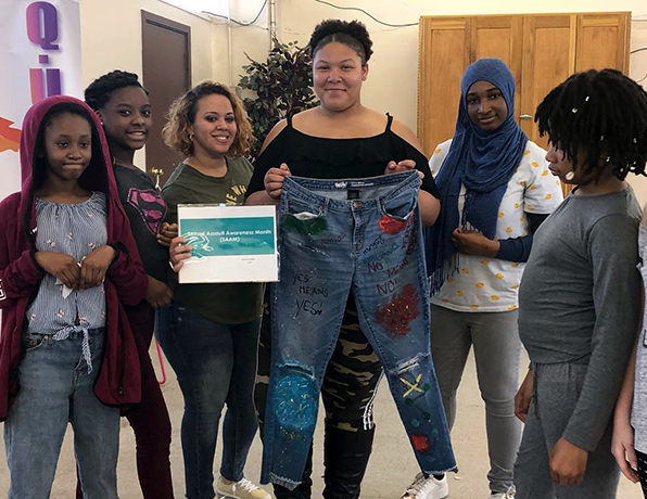 A group of young girls hold up a pair of decorated jeans.