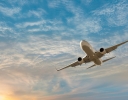 a plane glides in a shispy cloud sky with the sun dipping in the bottom left hand corner of the photo