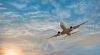 a plane glides in a shispy cloud sky with the sun dipping in the bottom left hand corner of the photo